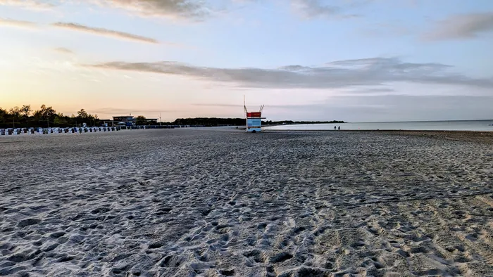 Breiter Sandstrand am Damp Südstrand am Abend, in der Mitte der Rettungsturm der DLRG, links eine Reihe Strandkörbe, rechts das flache Wasser