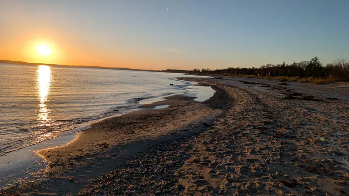 Strand bei Karlsminde im Winter bei tief stehender Sonne, das Licht spiegelt sich auf dem ruhigen Wasser der Eckernförder Bucht, am Spülsaum Steine und Tang